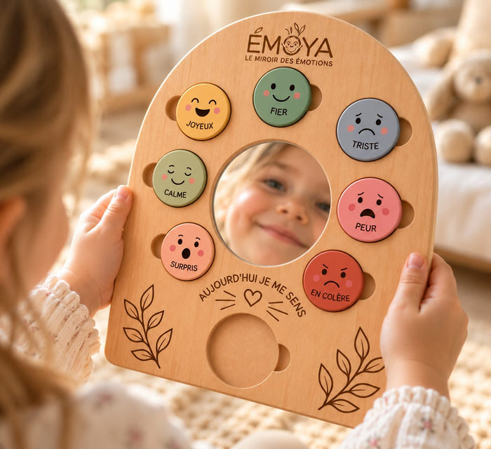 Un enfant tient le miroir des émotions ÉMOYA à deux mains et se regarde dans le miroir, entouré des jetons colorés