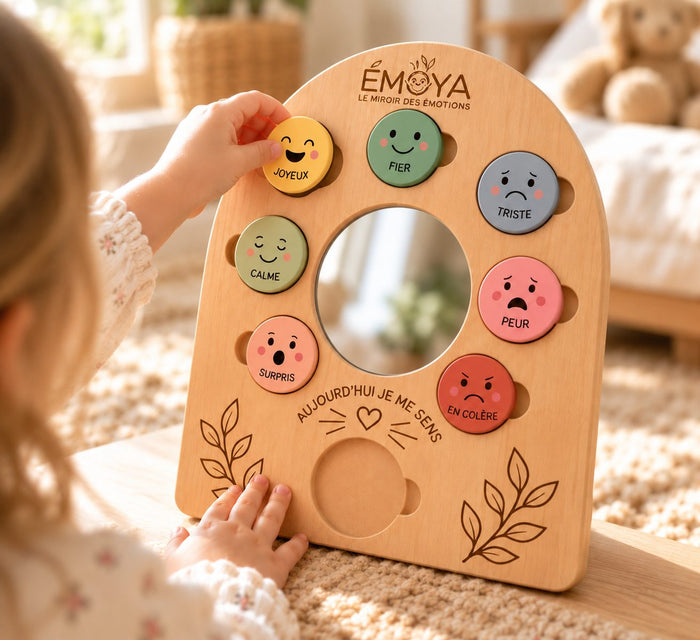 La main d'un enfant retire un jeton jaune « Joyeux » du support en bois du miroir ÉMOYA